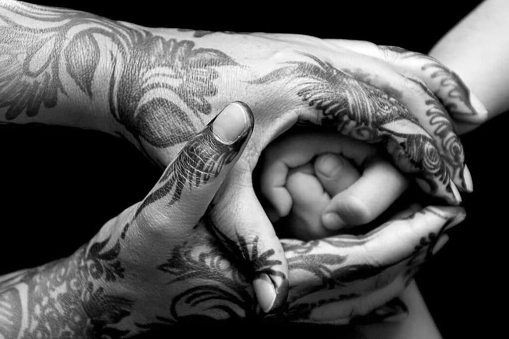 Two sets of hands that are wrapped around each other in prayer. One set of hands has Indian style henna designs.