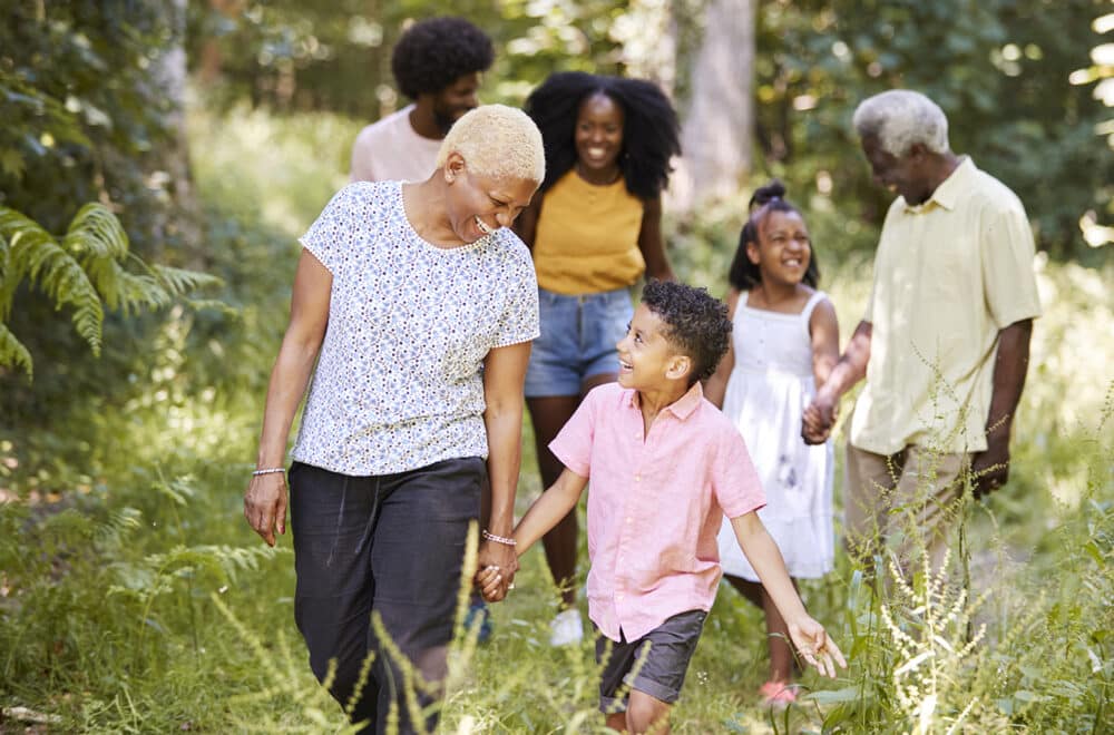 Senior black woman walking with smiling grandson and family in woods.