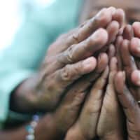 Three pairs of hands that are folded in prayer over eachother in agreement.