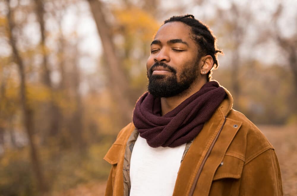 A man practicing silencing by standing in the forest with his eyes closed during the fall season.