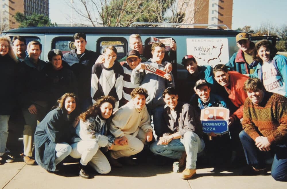 College students pose for an image in front of the Nav Van on a college campus.