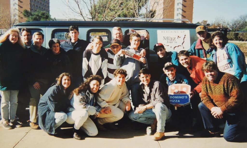 College students pose for an image in front of the Nav Van on a college campus.