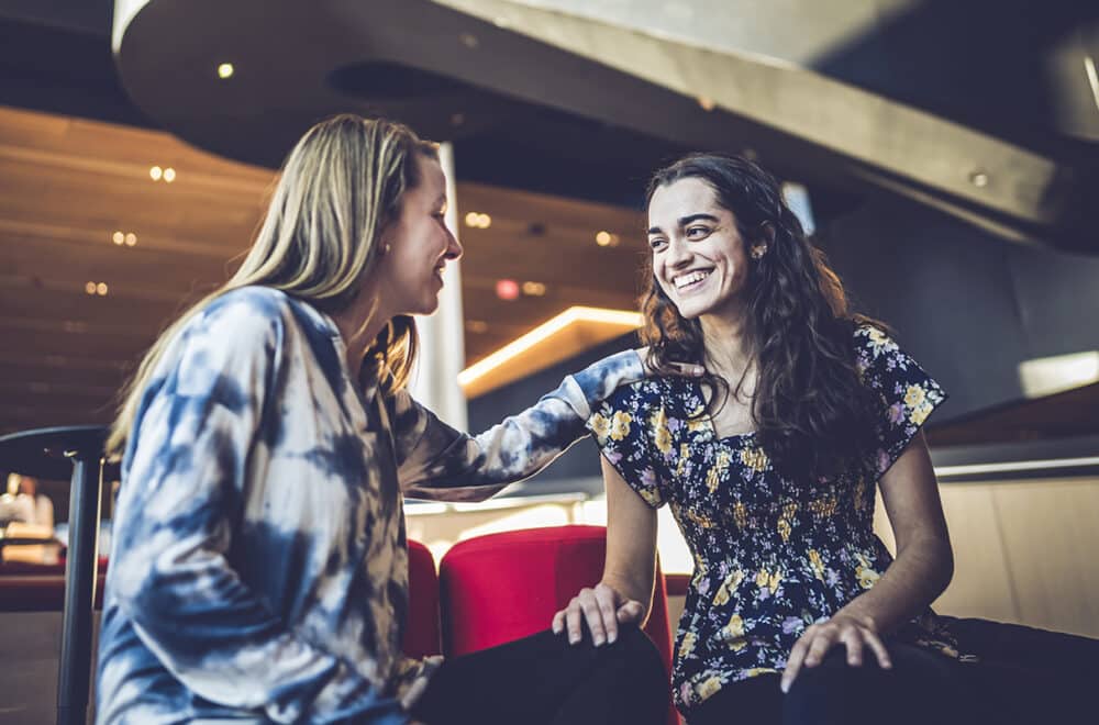 Sophia meeting with a friend in a coffee shop with a dark background and low lighting.