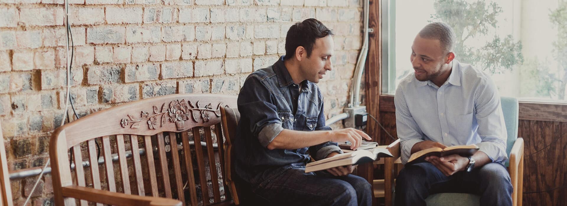 Two men sit on a bench, reading the Bible together.