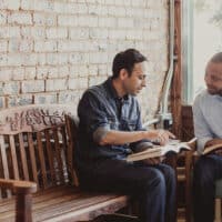 Two men sit on a bench, reading the Bible together.